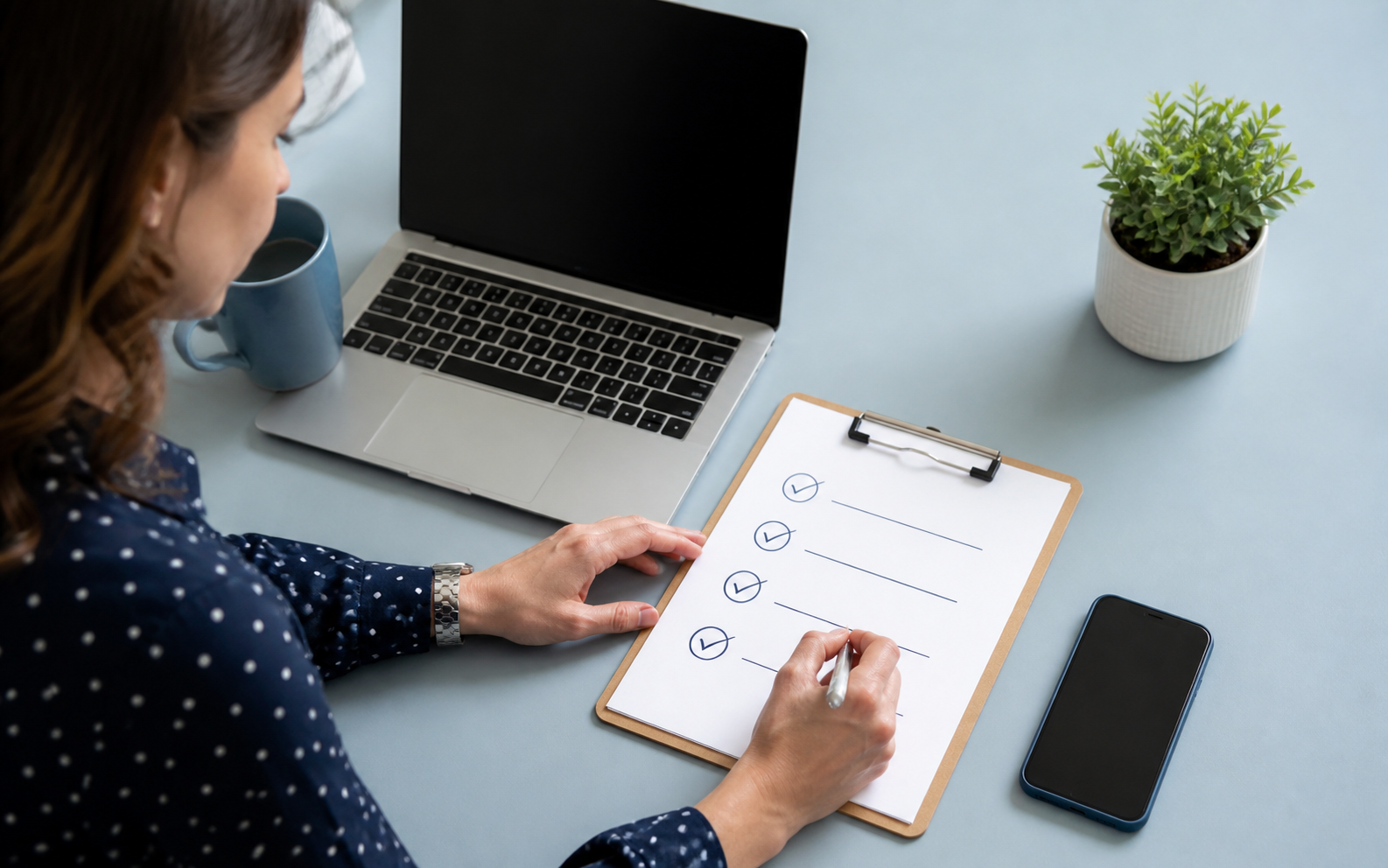 Office manager checking cybersecurity tasks on a clipboard beside a laptop